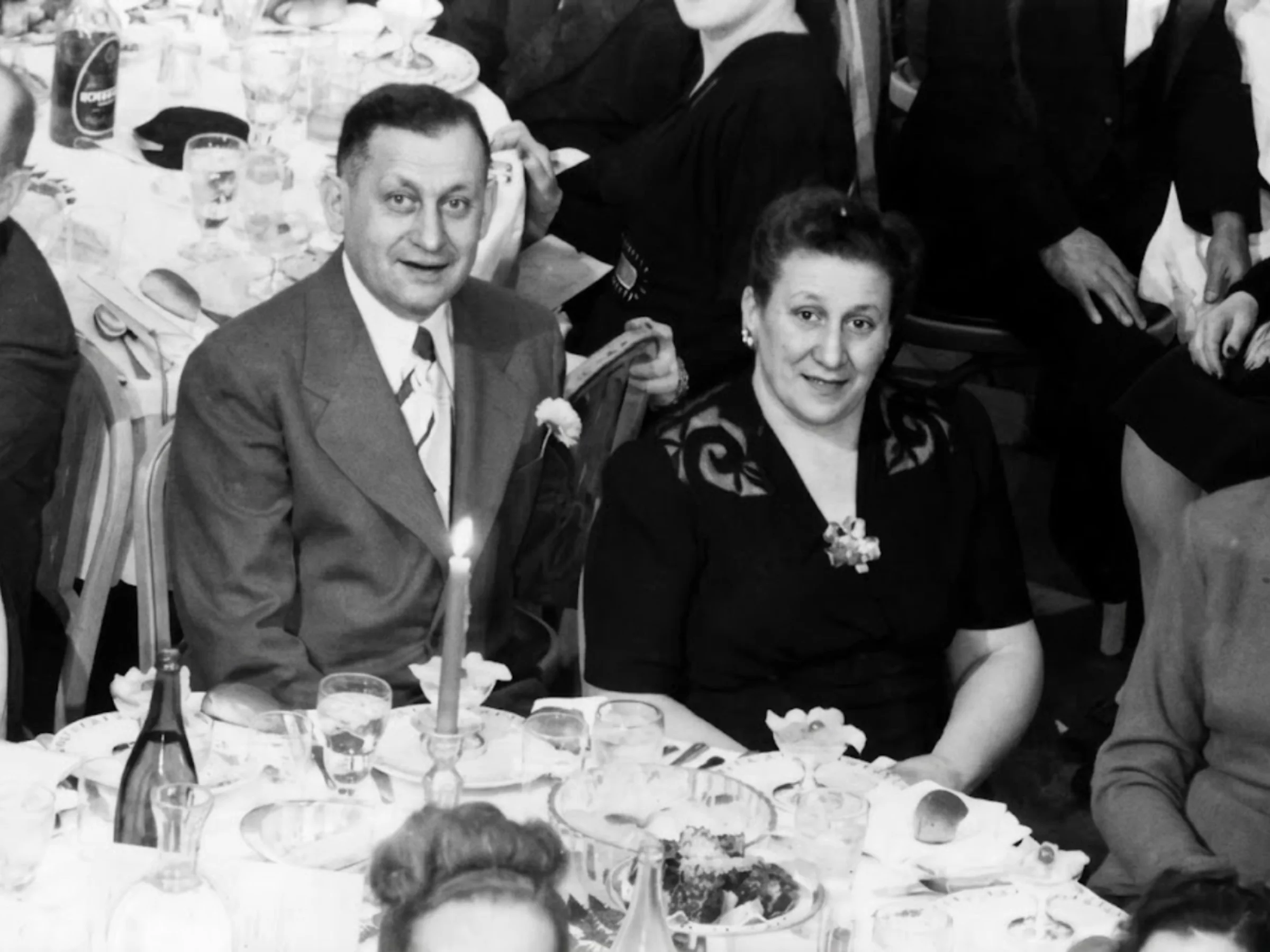 Black and white mid-20th-century photo of a light-skinned man and a woman in formal attire seated together at a round table at a social function.