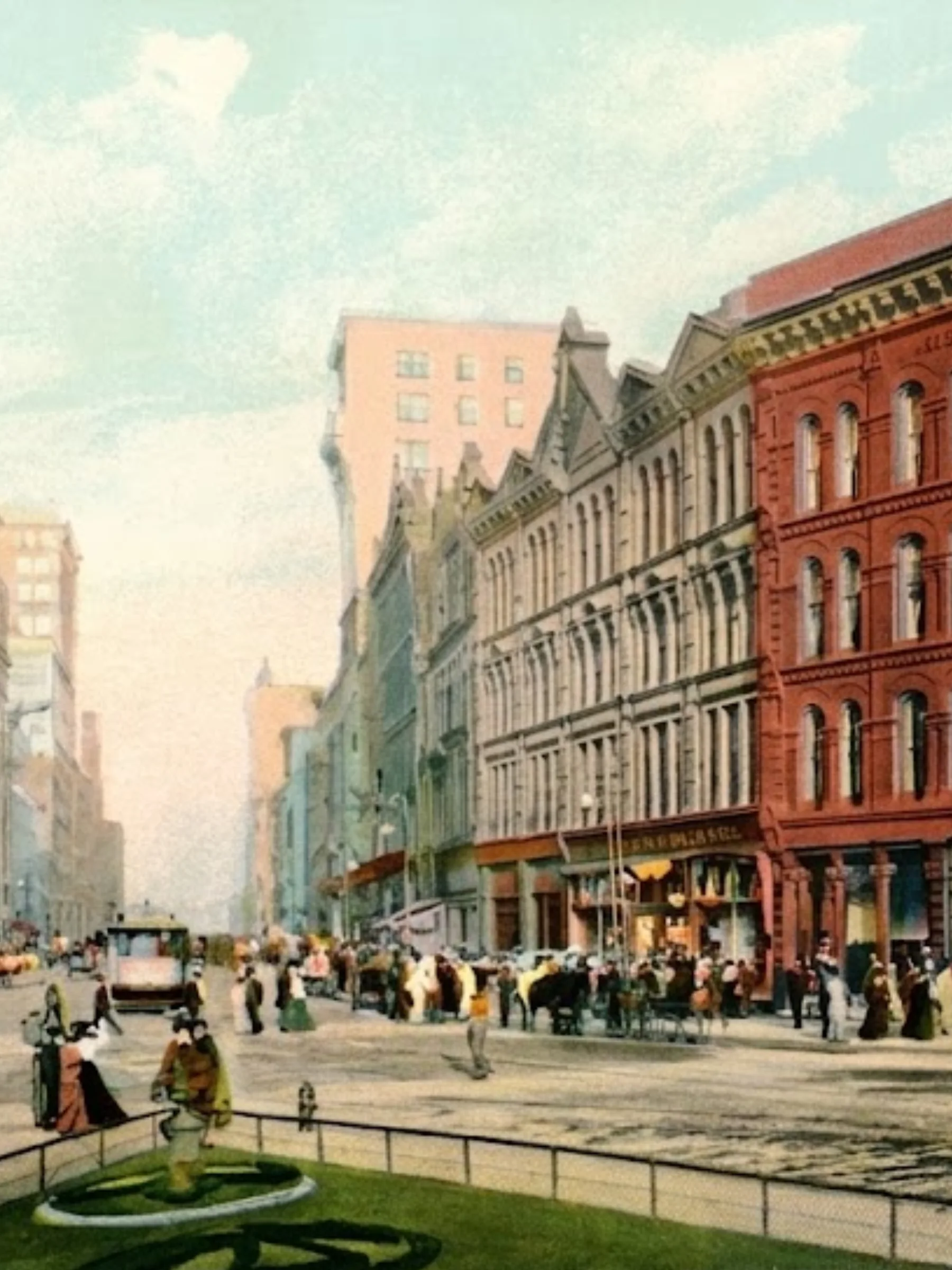 Colorized vintage postcard or lithograph from the early 1900s of a bustling street scene. Multi-story building fronts line the street. There are people and horse-drawn carriages throughout. The edge of a green space is in the foreground.